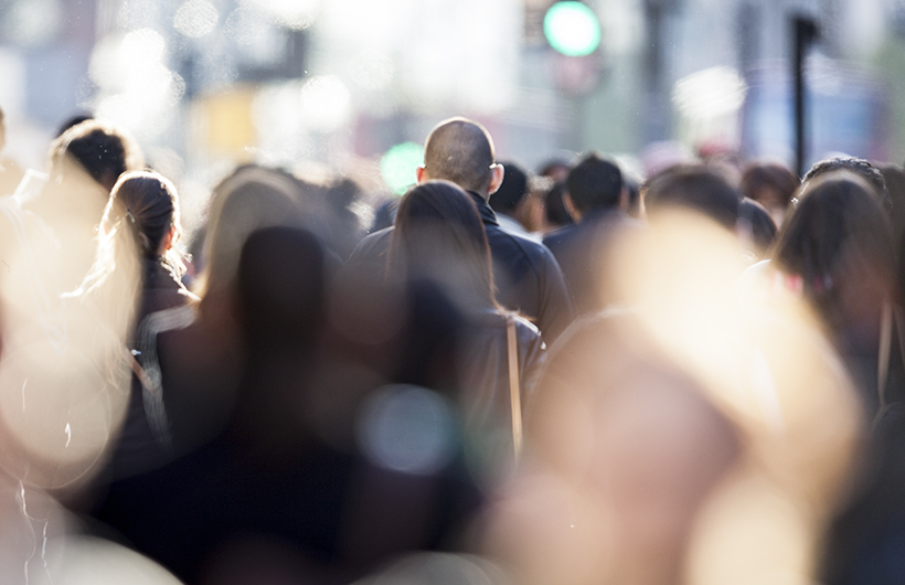 heads of people walking within a crowd outside. Closer silhouettes are out of focus. 
