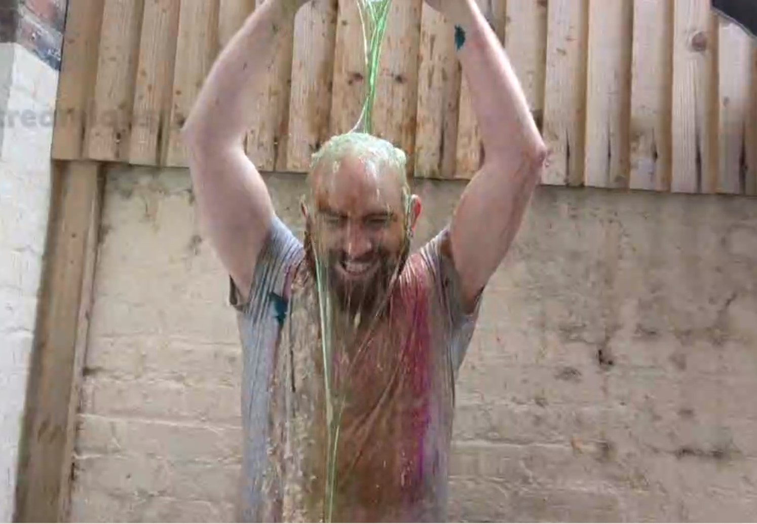 Jinjar - bearded streamer in grey t shirt pours lime green slime over his head, previous slime/beans/chaos can be seen on his t shirt already.