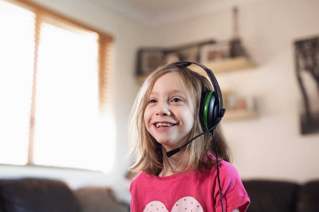 A young child with headset smiling in a pink t shirt