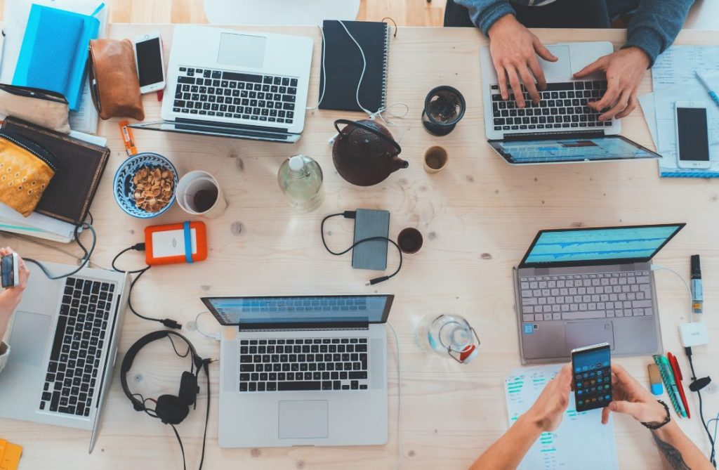 a top down view of a table filled with laptops, headphones, cups and office work related items 