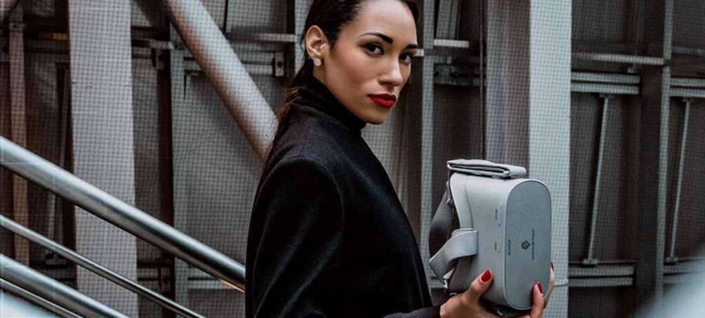 A woman wearing black holding a VR headset and looking towards the camera