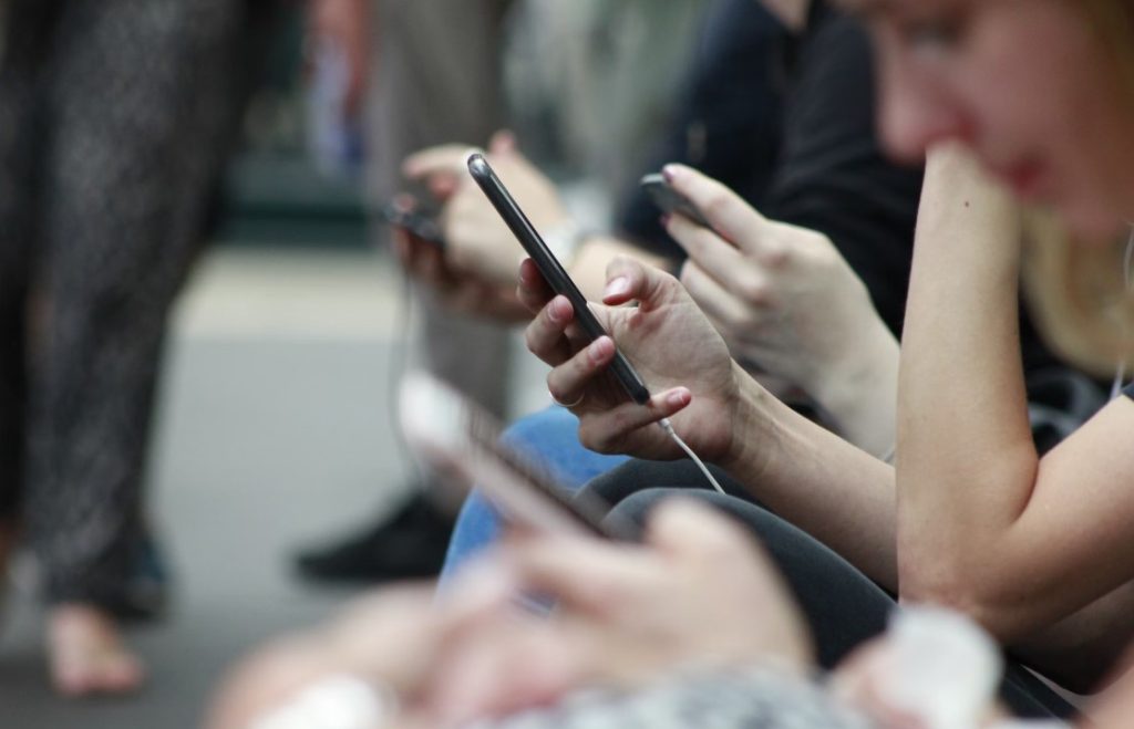 several hands holding phones whilst on a bench outside
