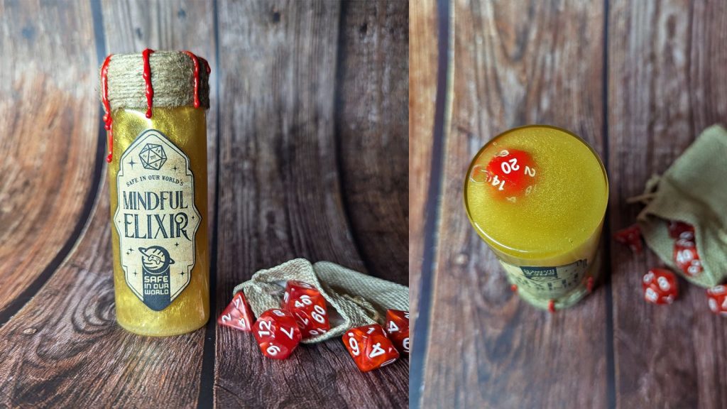 a gold liquid dice shaker with red dice, and a label on the front reading "Safe In Our World's Mindful Elixir"