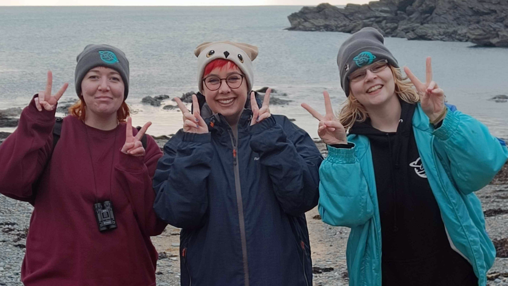 Three members of the Safe In Our World on a beach in Wales, celebrating the success of the charity bundle 2025.