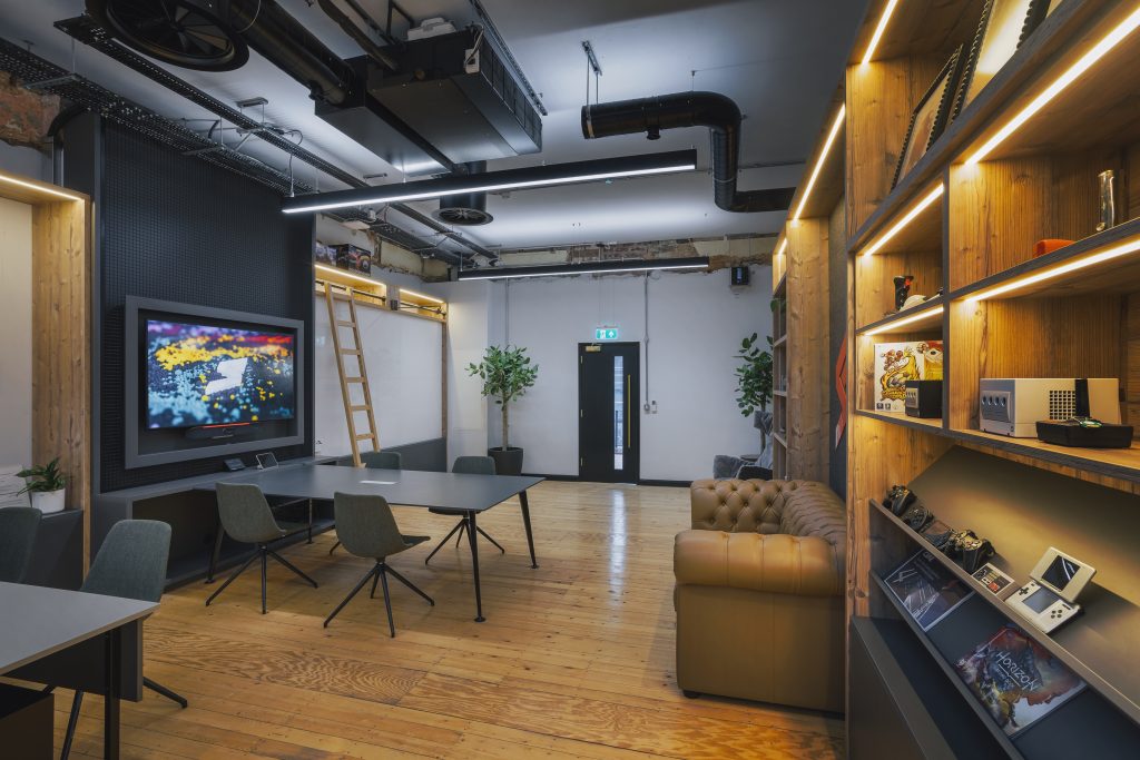 Workplace design example from Claremont, with wooden floors, sofas and desks beside large screens.