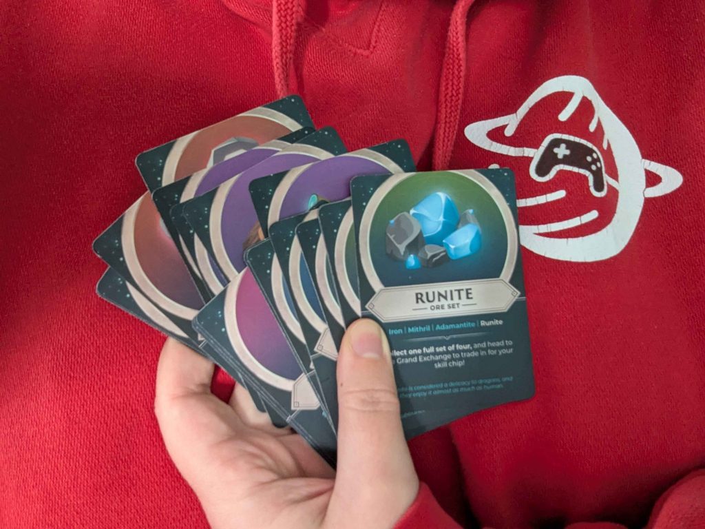 A handful of trading cards from RuneFest 2025, against a red Safe In Our World hoodie.